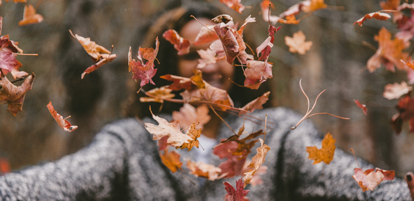 Dried leaves are falling down in front of a woman.