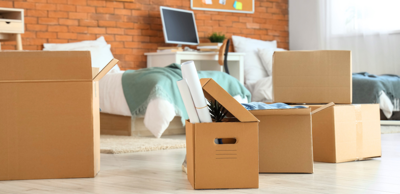 A bedroom with a computer and a couple of boxes scattered.