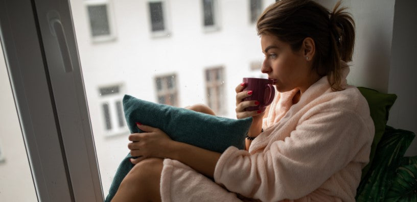 A woman with her bathrobe on is drinking a cup of coffee.