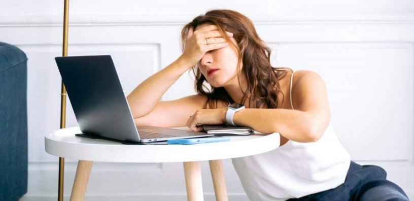 A woman looks very tired in front of her laptop.