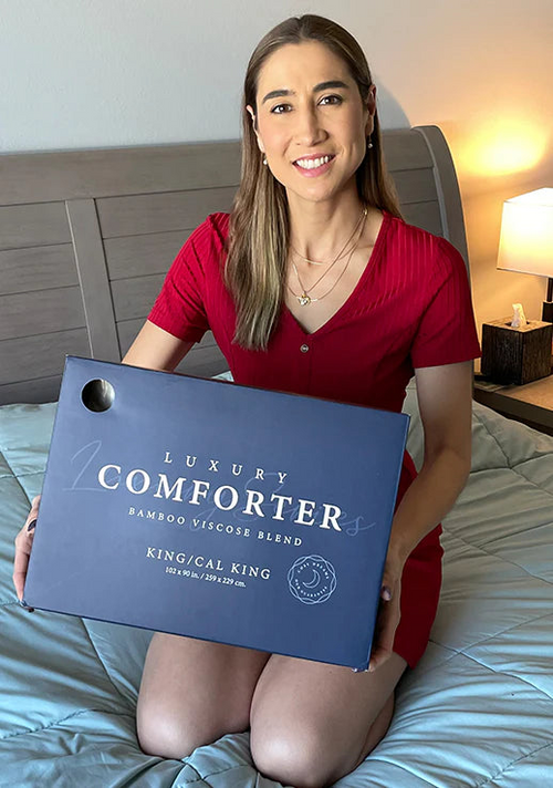 A customer is comfortably sitting down on her bed displaying her new Luxury Down Alternative Comforter.