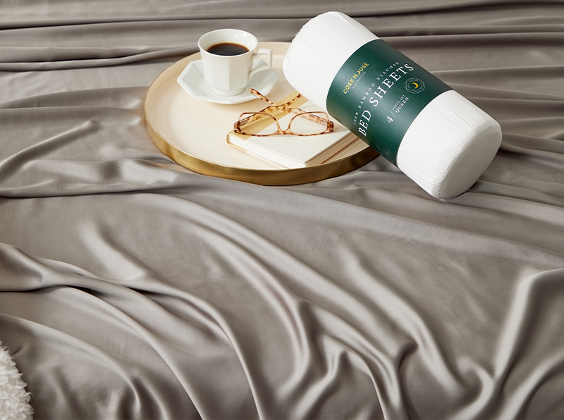 A cup of coffee on a tray with a packaged set of Cosy House Collection’s 100% Bamboo sheets on a bed.