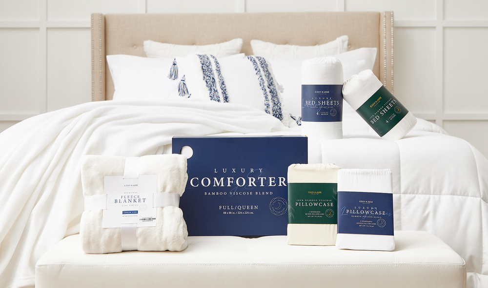 A bed with Cosy House Collection sheet sets, pillows, pillowcases, comforters, and blankets.