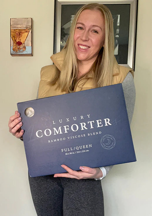 A standing and smiling customer flexes her packaged Luxury Down Alternative Comforter.