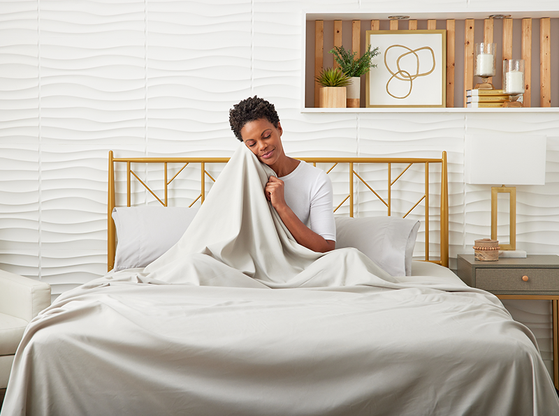 A woman is seated on a bed with Cosy House Collection bedding, exuding a sense of relaxation and tranquility.