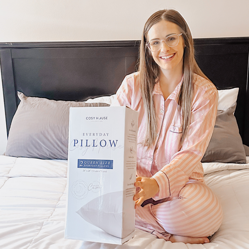 Another happy customer sitting on the bed showing a packaged pair of Everyday Down Alternative Pillows.