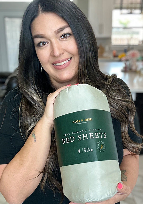 A happy customer is holding a packaged set of Cosy House Collection’s 100% Bamboo sheets.