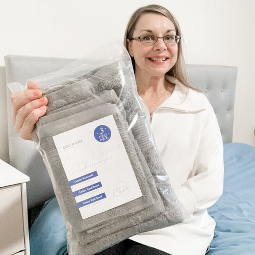 A happy customer sitting on her bed showing her new Essential Cotton Towel set.