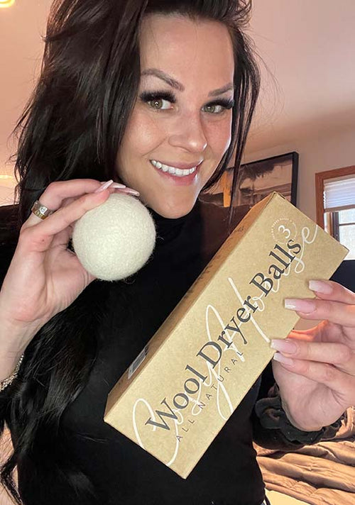 A smiling customer flexing her Cosy House Collection All Natural Wool Dryer Balls.