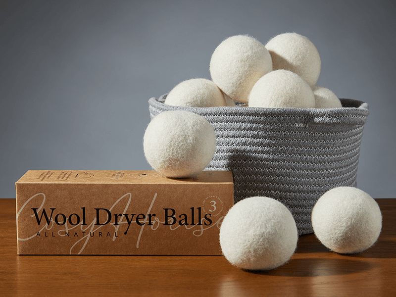 Cosy House Collection’s All Natural Wool Dryer Balls in its original packaging and some are in a basket.