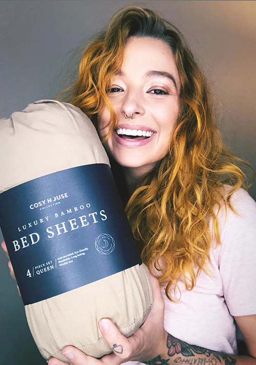 A happy customer is holding a packaged set of Cosy House Collection’s Luxury bed sheets.